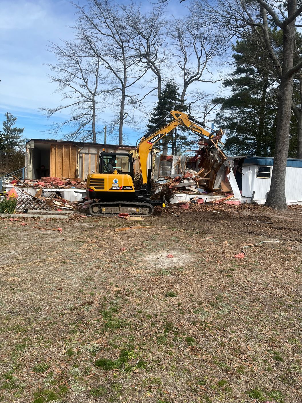 A yellow excavator is demolishing a house in a field.