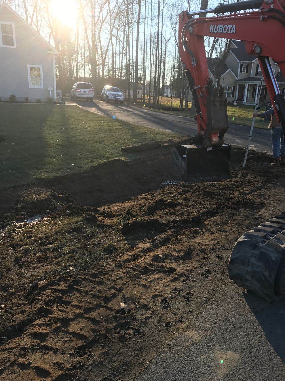An excavator is digging a hole in the dirt in front of a house.