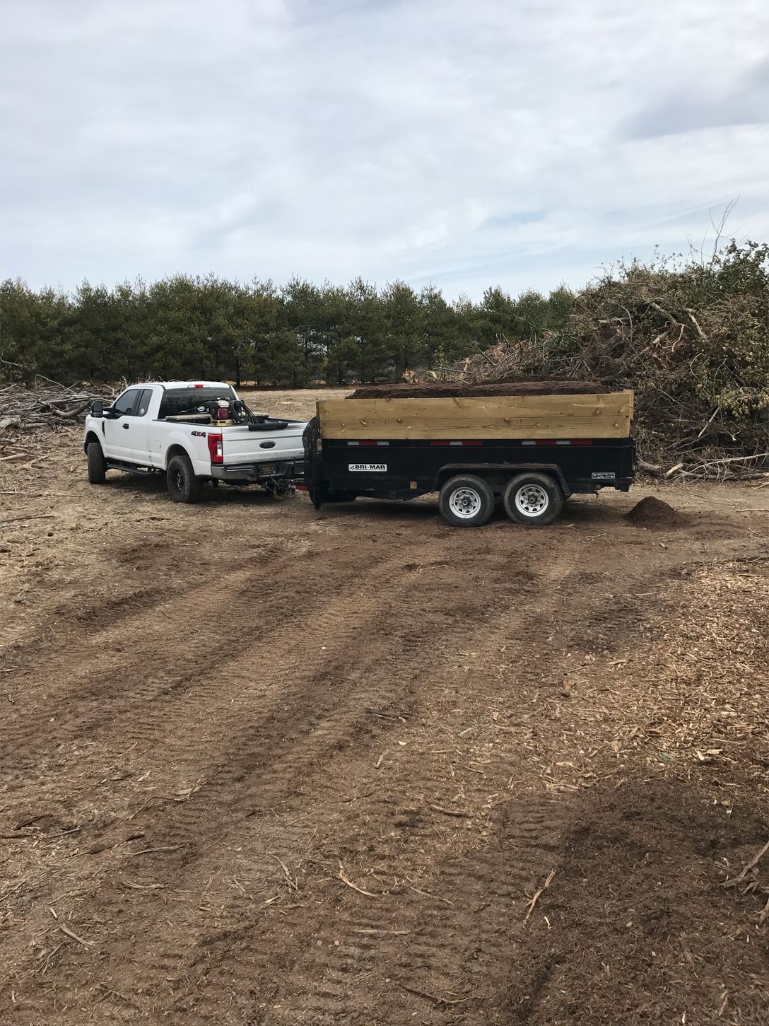 A white truck is towing a dump trailer in a dirt field.
