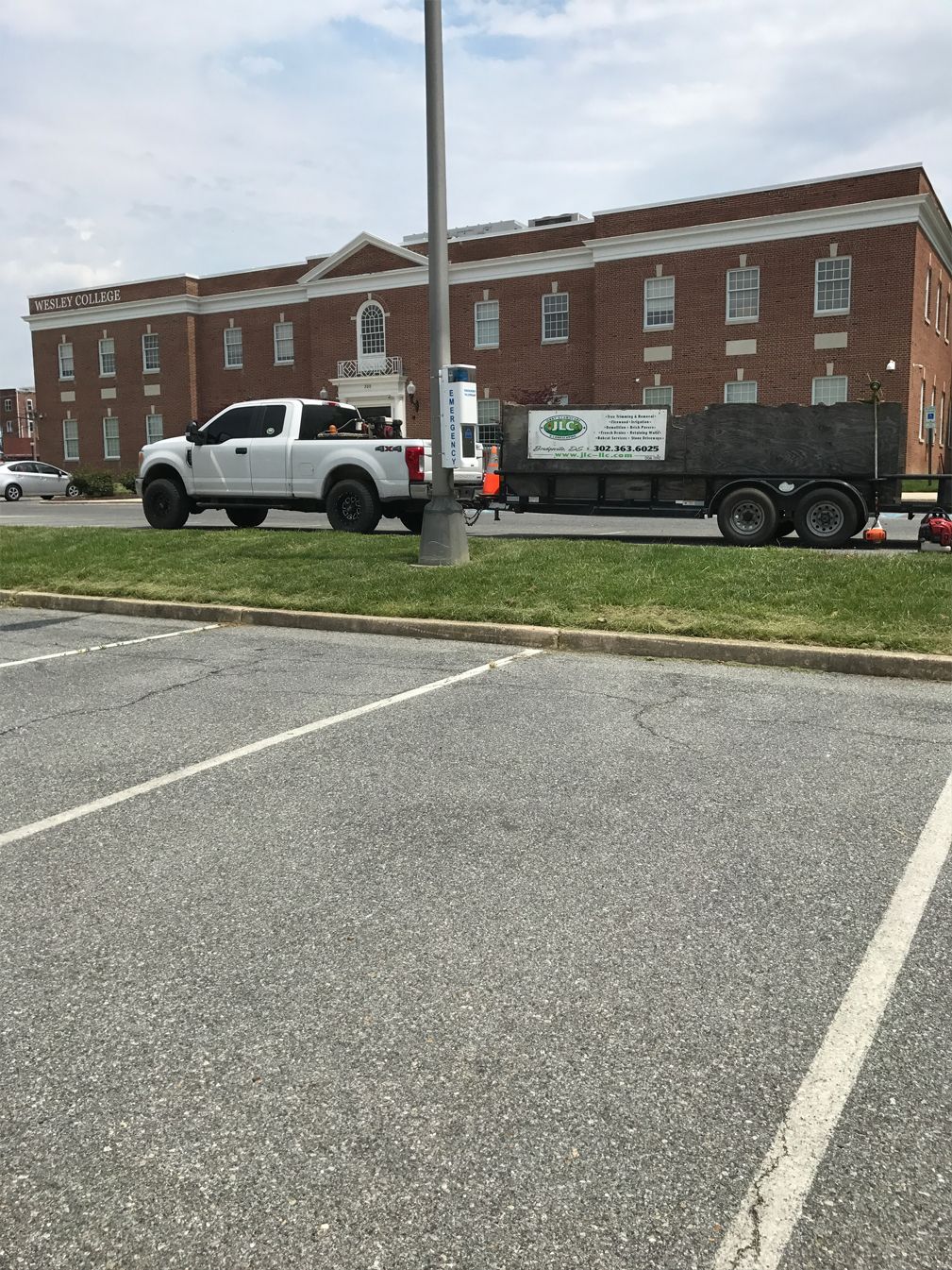 A truck and trailer are parked in a parking lot in front of a brick building.