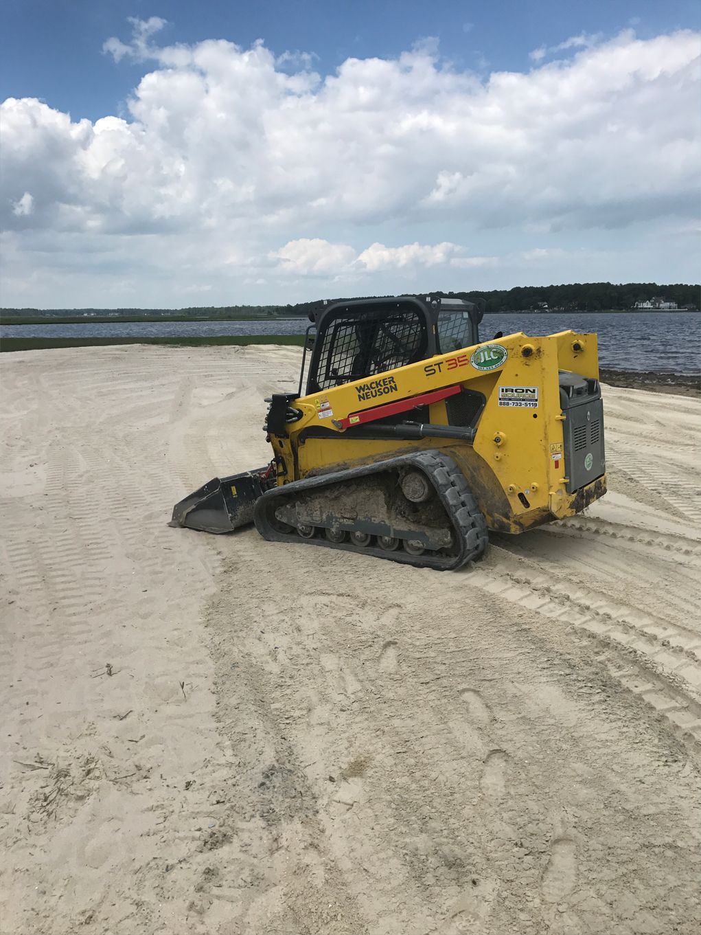 A yellow bulldozer is sitting on top of a sandy beach next to a body of water.