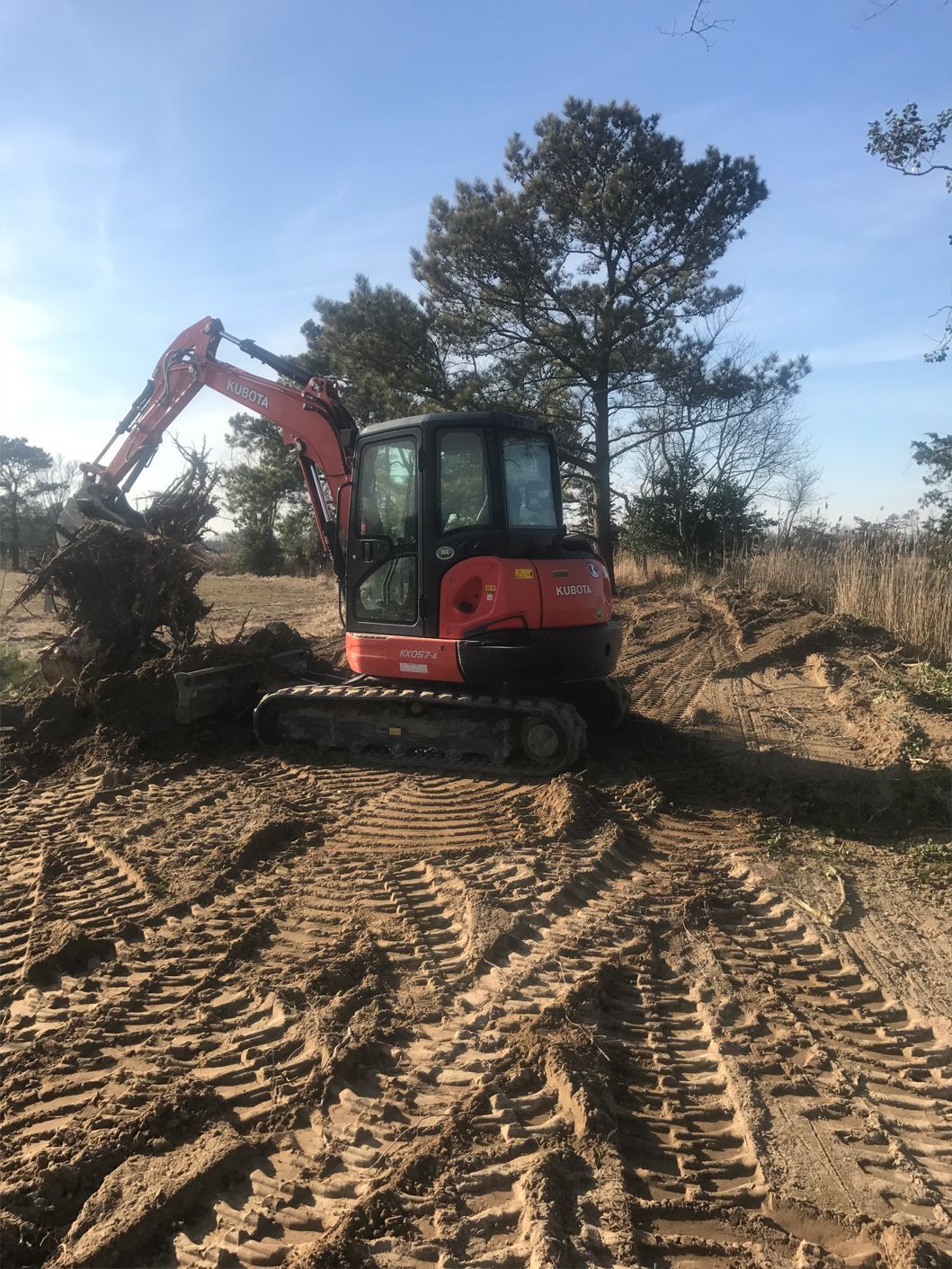 A red excavator is digging a hole in the dirt in a field.