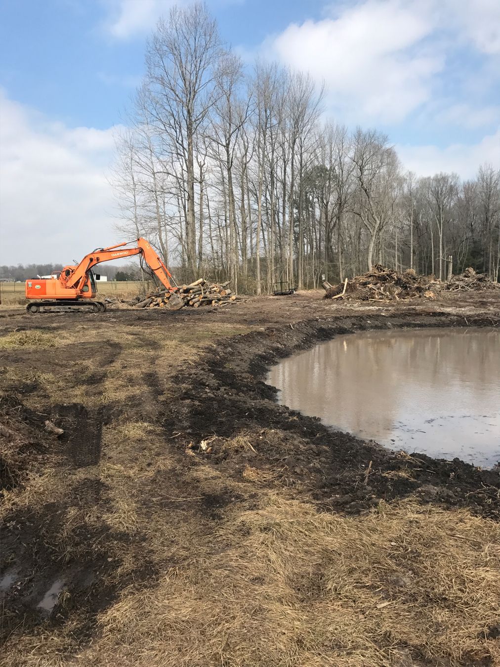 A large orange excavator is digging a pond in a field.