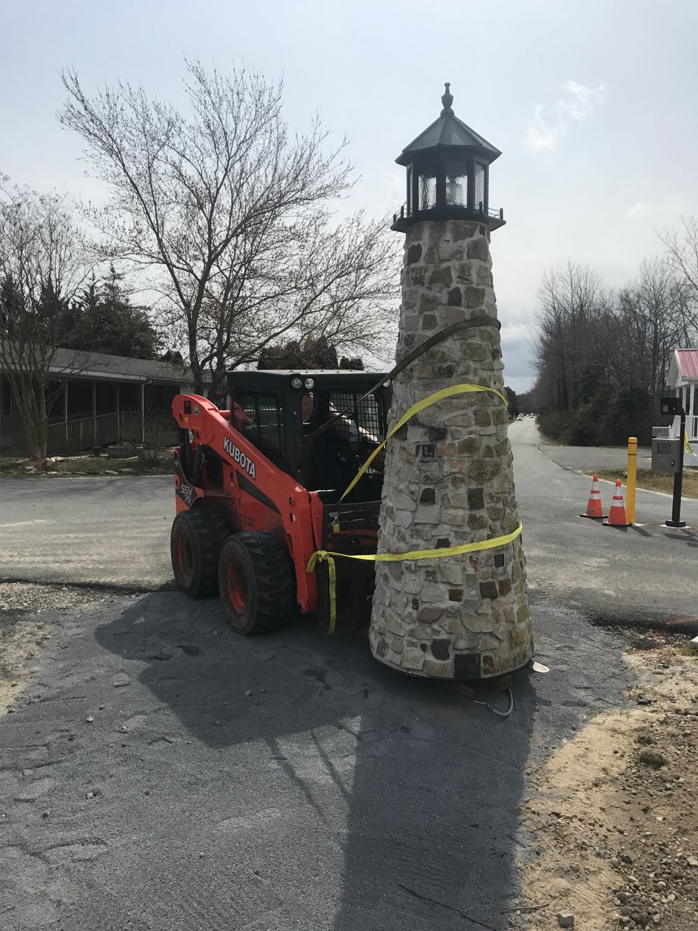 A small tractor is moving a large stone lighthouse on the side of the road.