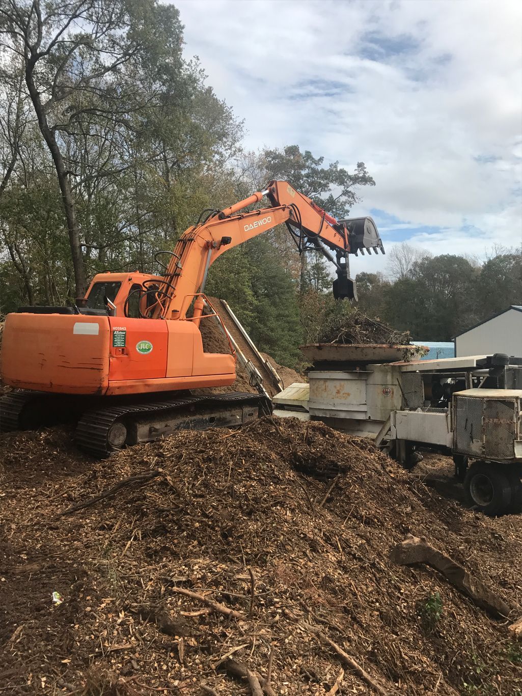 A large orange excavator is digging in a pile of wood chips.