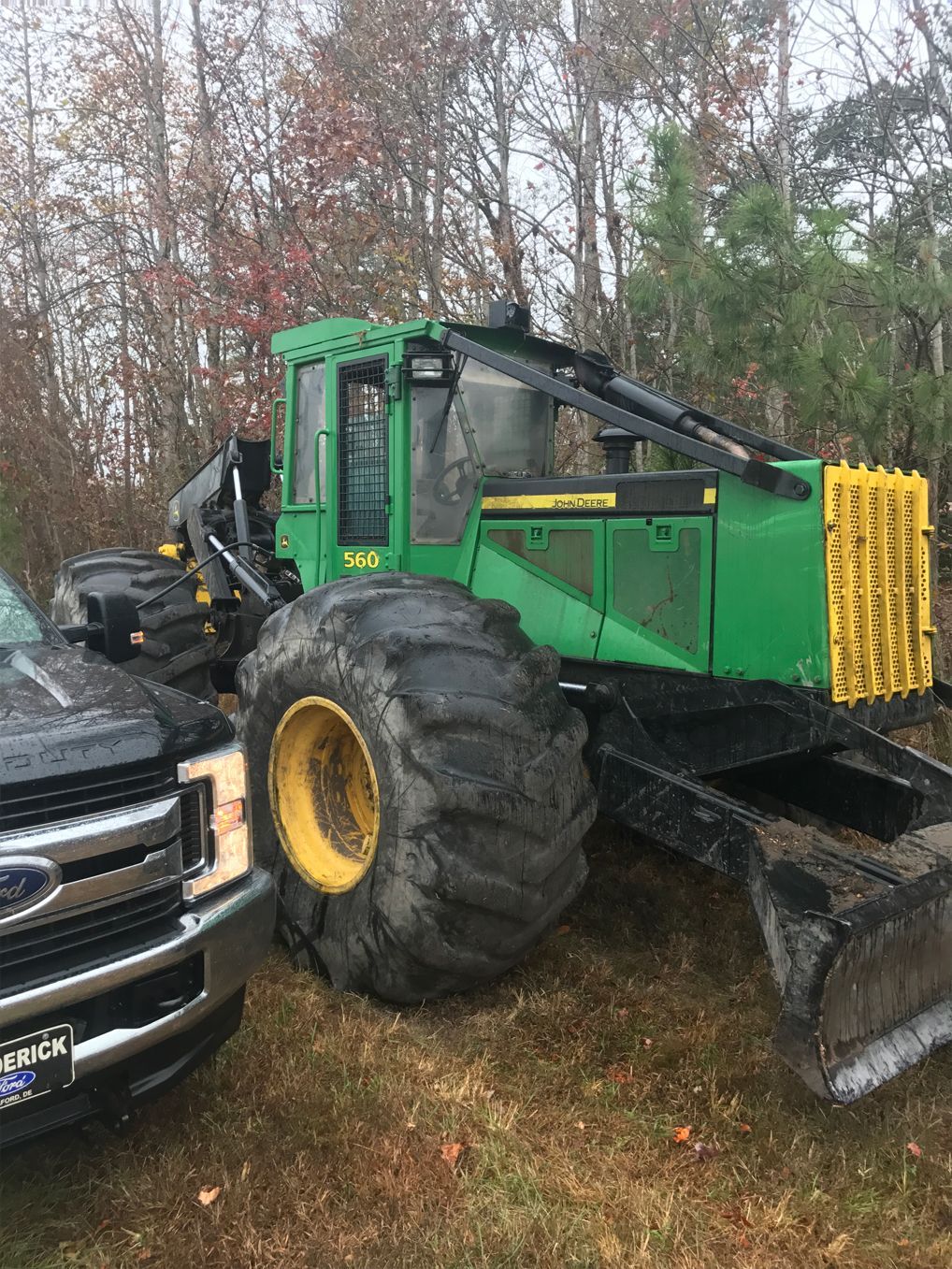 A green tractor is parked next to a black truck in a field.