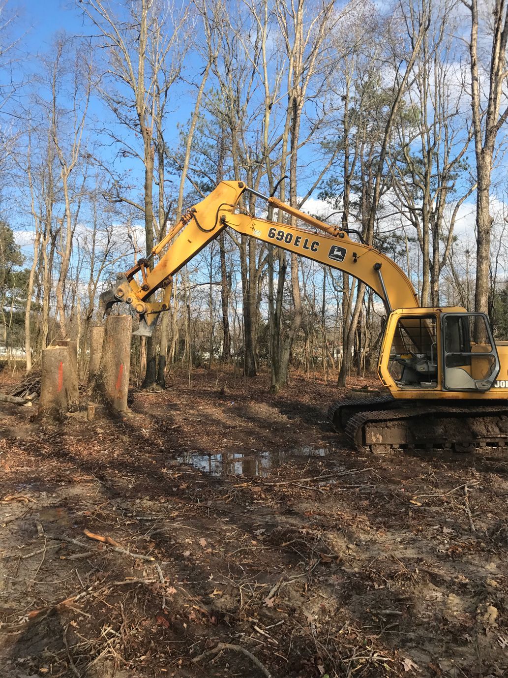 A yellow excavator is digging a hole in the middle of a forest.