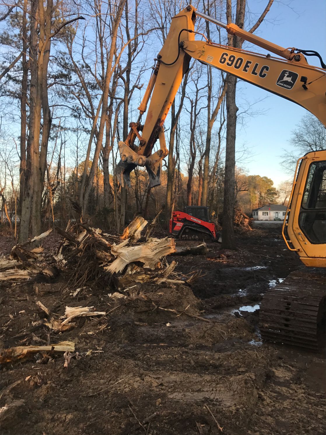 A yellow excavator is cutting down trees in a forest.