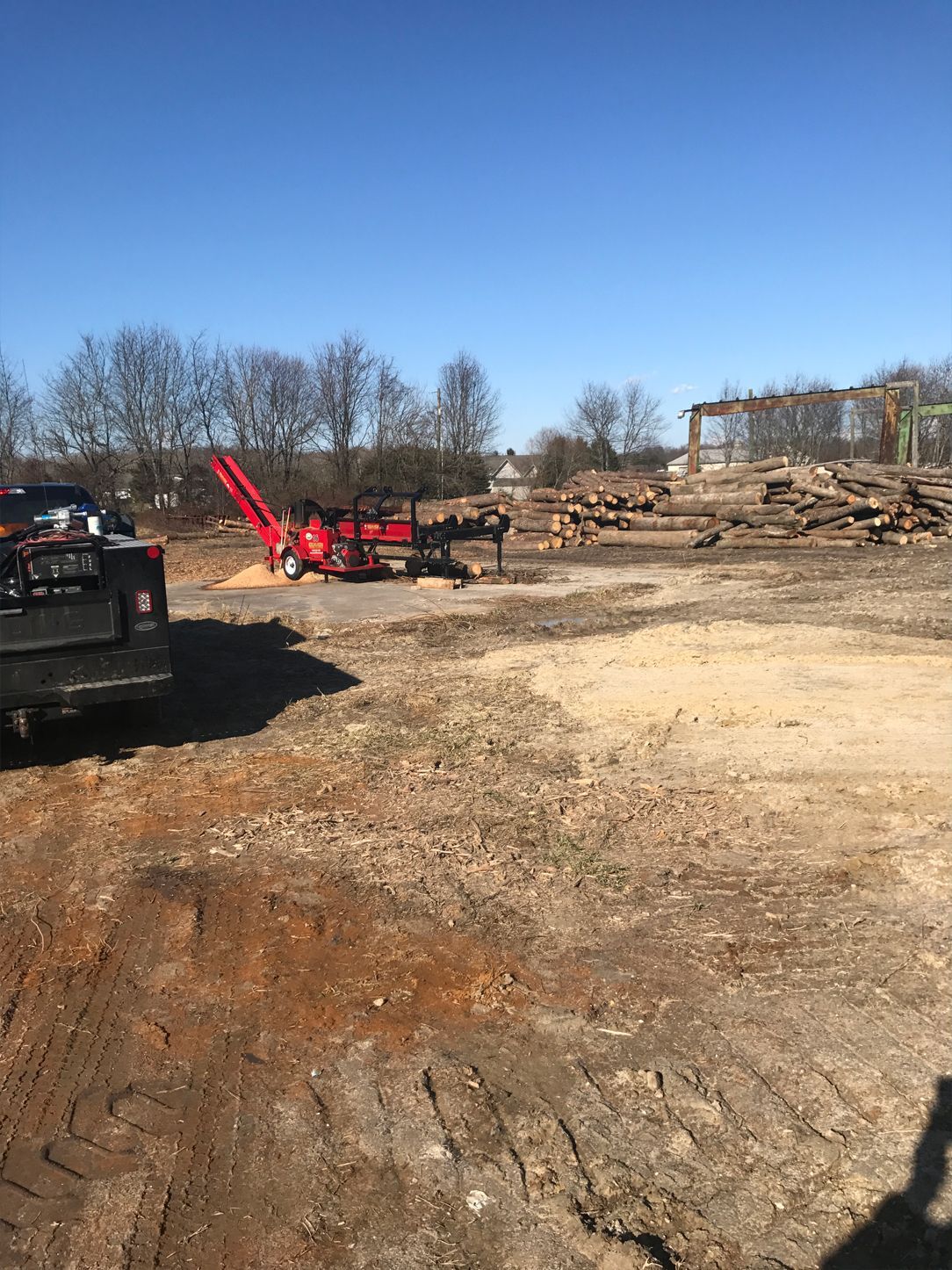A truck is parked in a dirt field next to a pile of logs.