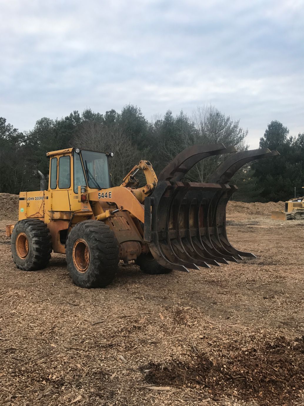 A yellow tractor is parked in a pile of wood chips in a field.