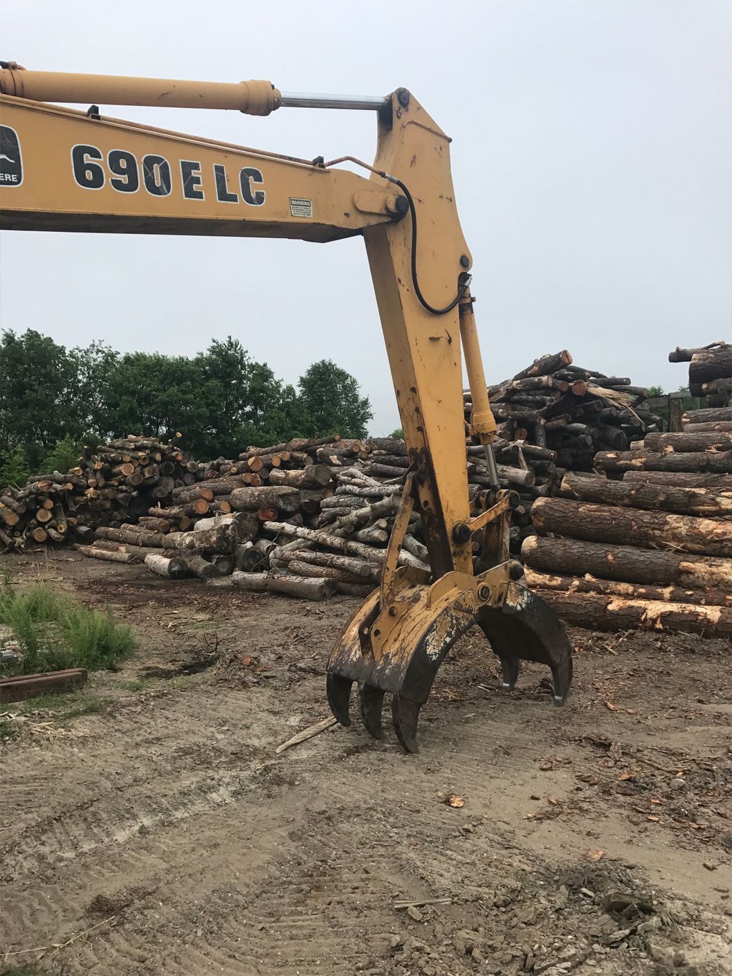 A yellow excavator is sitting in front of a pile of logs.