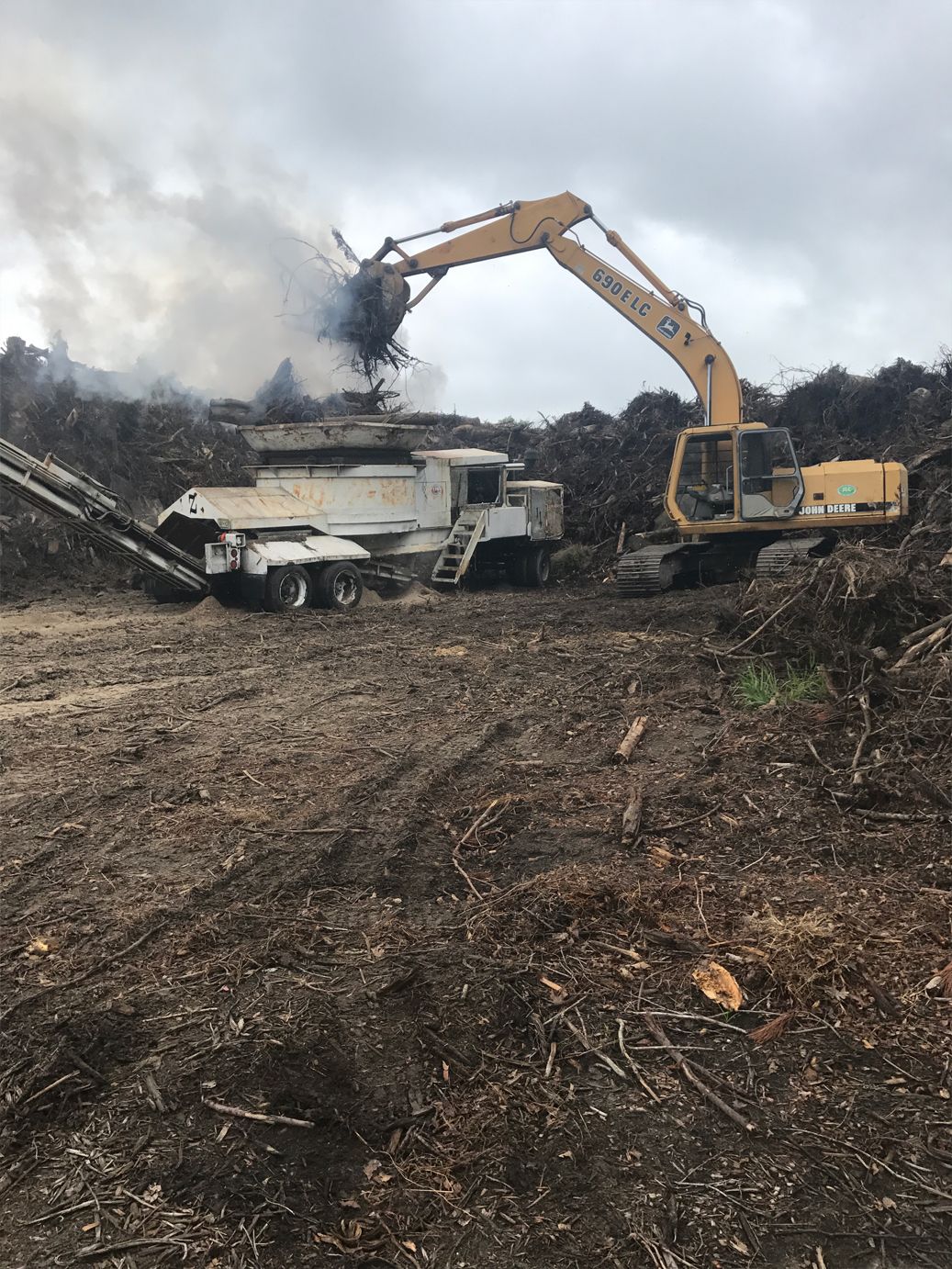 A large yellow excavator is working on a pile of wood chips.
