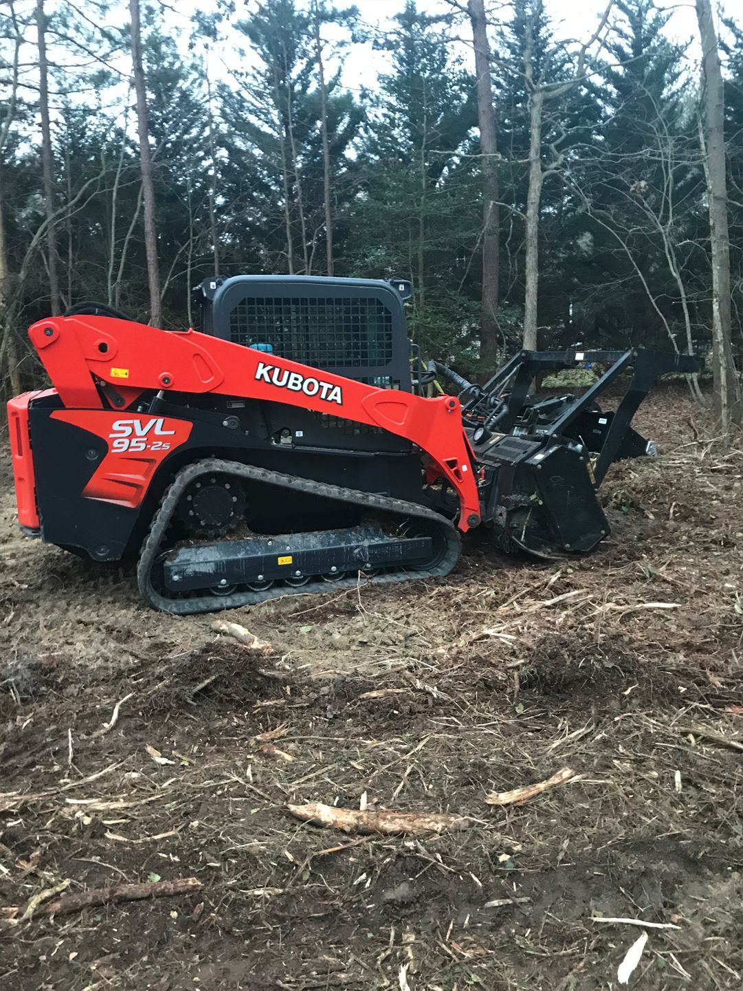 A red and black skid steer is sitting in the middle of a forest.