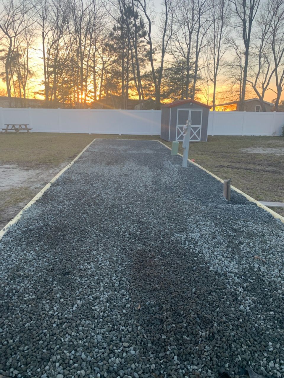 A gravel driveway leading to a shed with a sunset in the background.