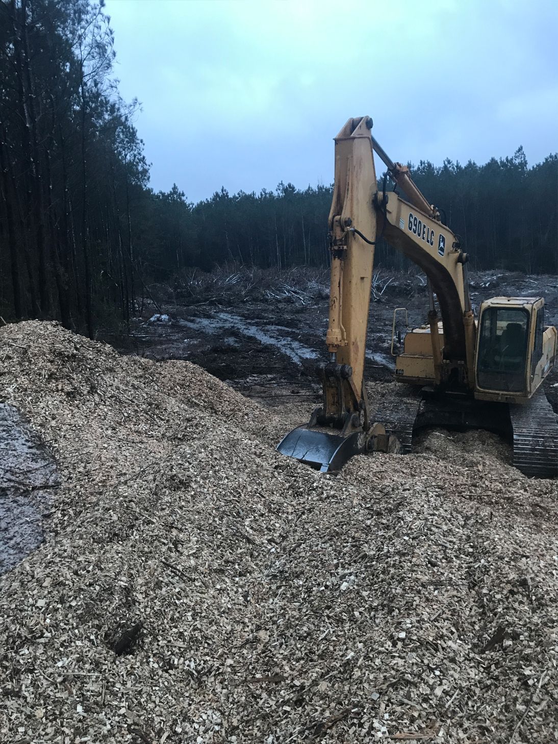 A yellow excavator is digging in a pile of wood chips.