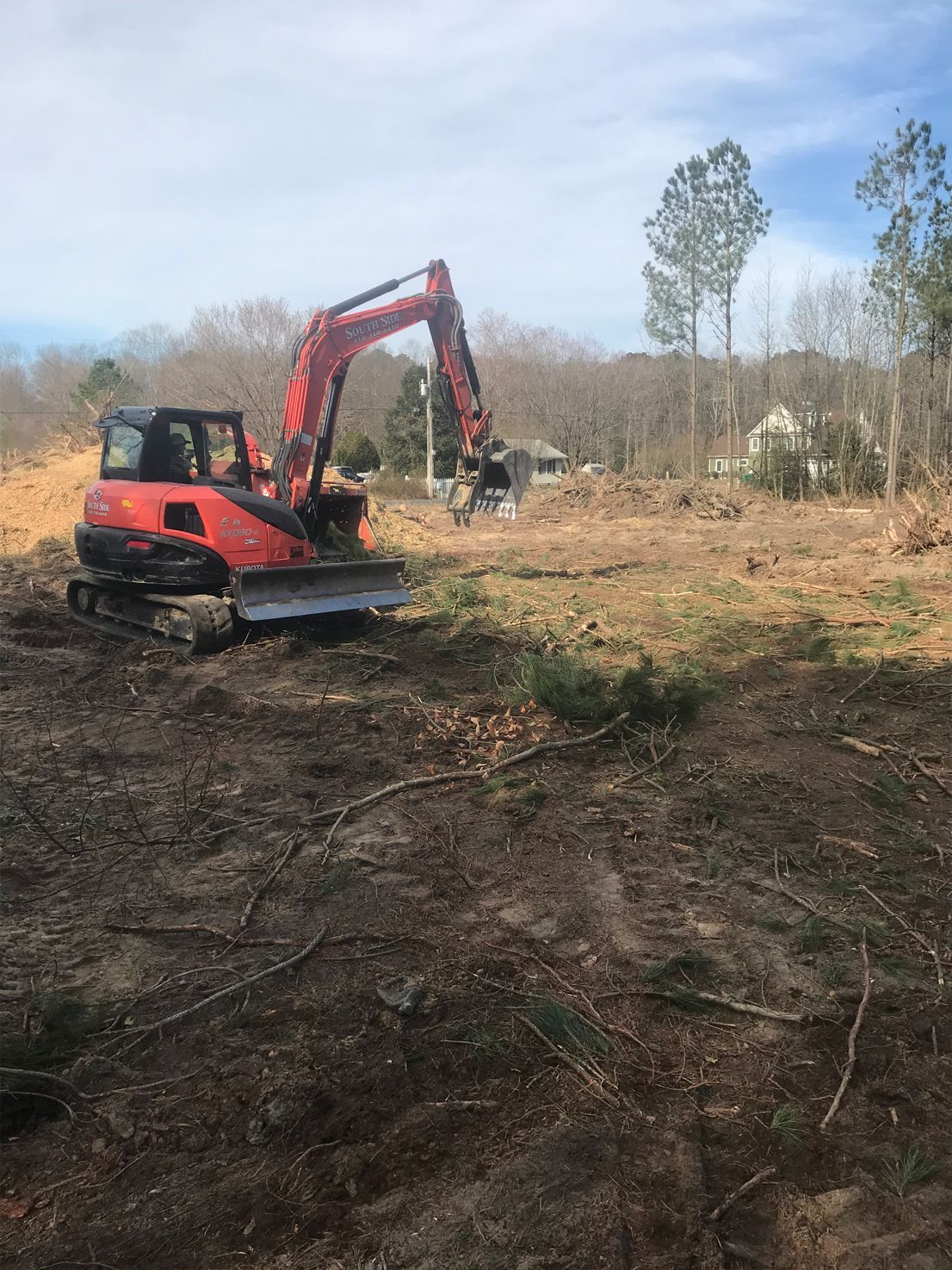 A red excavator is moving dirt in a field.