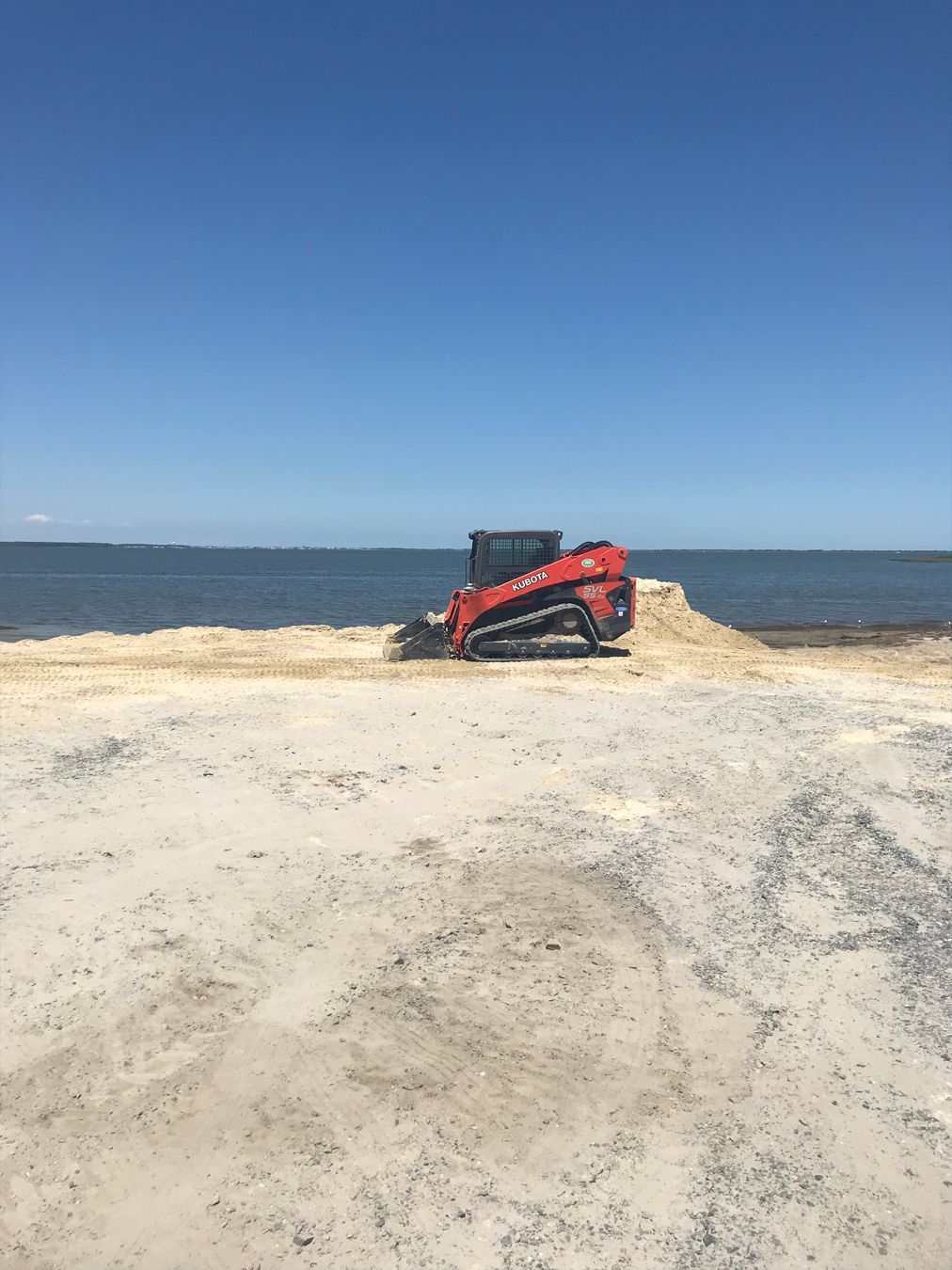 A bulldozer is moving sand on a beach near the ocean.