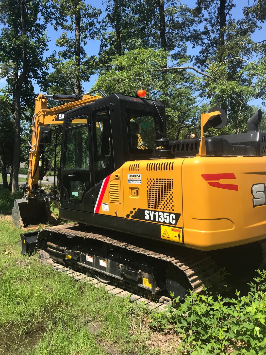 A yellow excavator is parked in the grass next to trees.