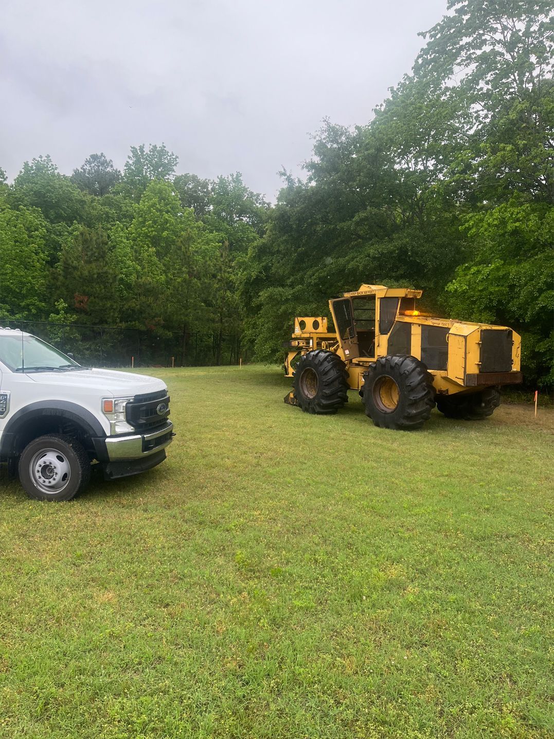 A white truck is parked next to a yellow tractor in a grassy field.