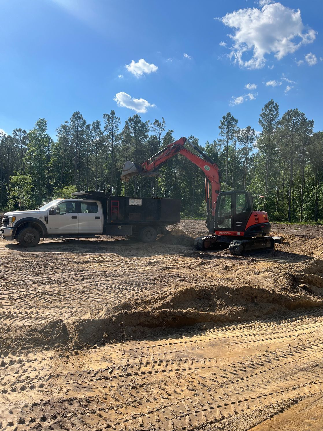 A white truck is being towed by an excavator in a dirt field.