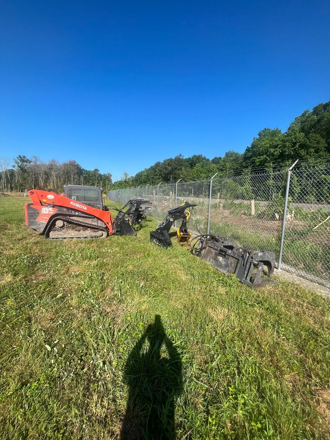 A group of tractors are parked in a grassy field next to a fence.