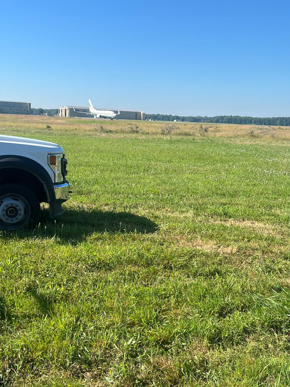 A white truck is parked in a grassy field with a plane in the background.