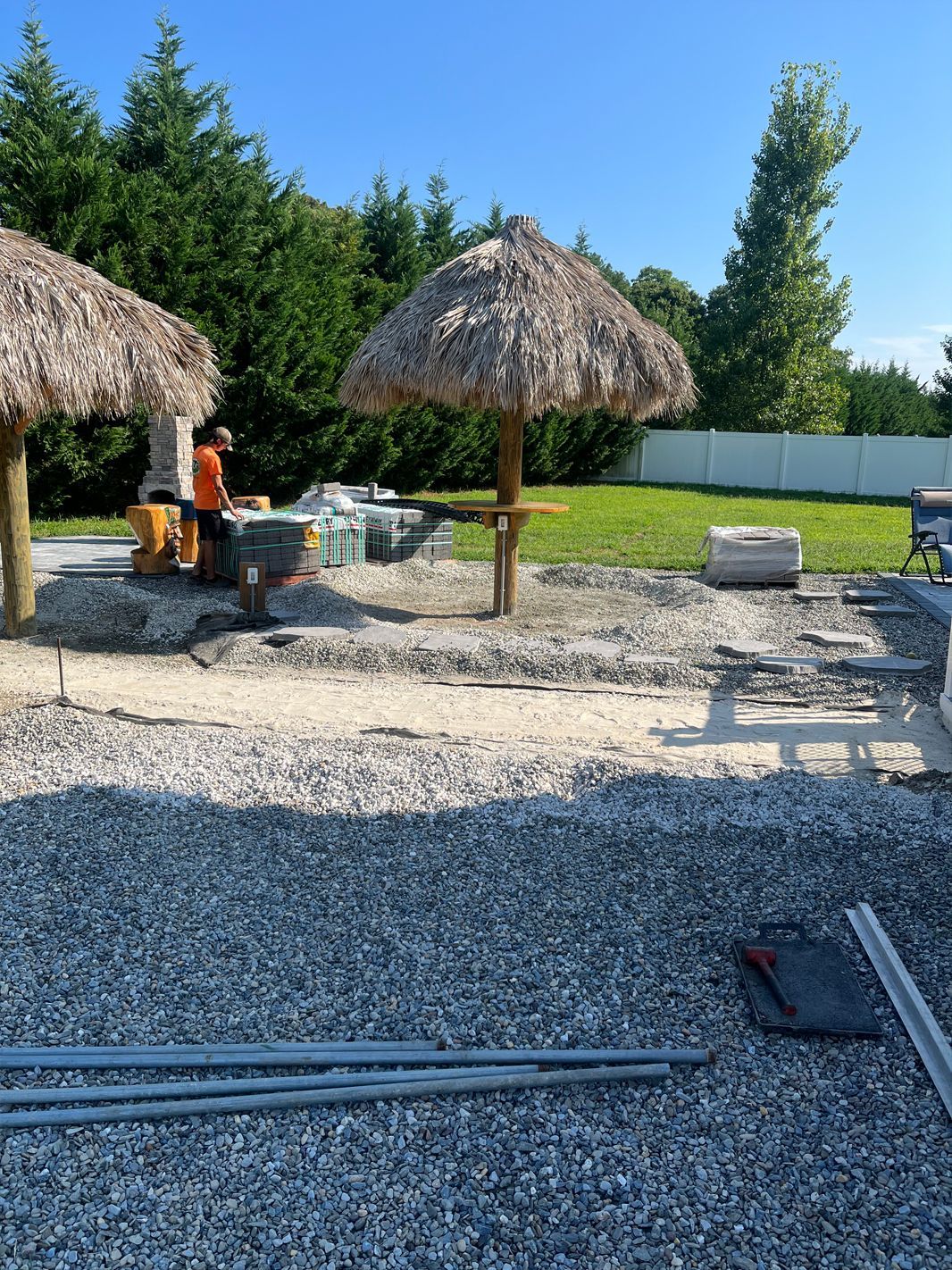 A man is sitting under an umbrella in a gravel yard.