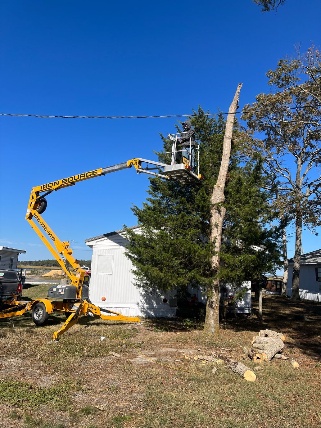 A man is cutting a tree with a crane in front of a house.