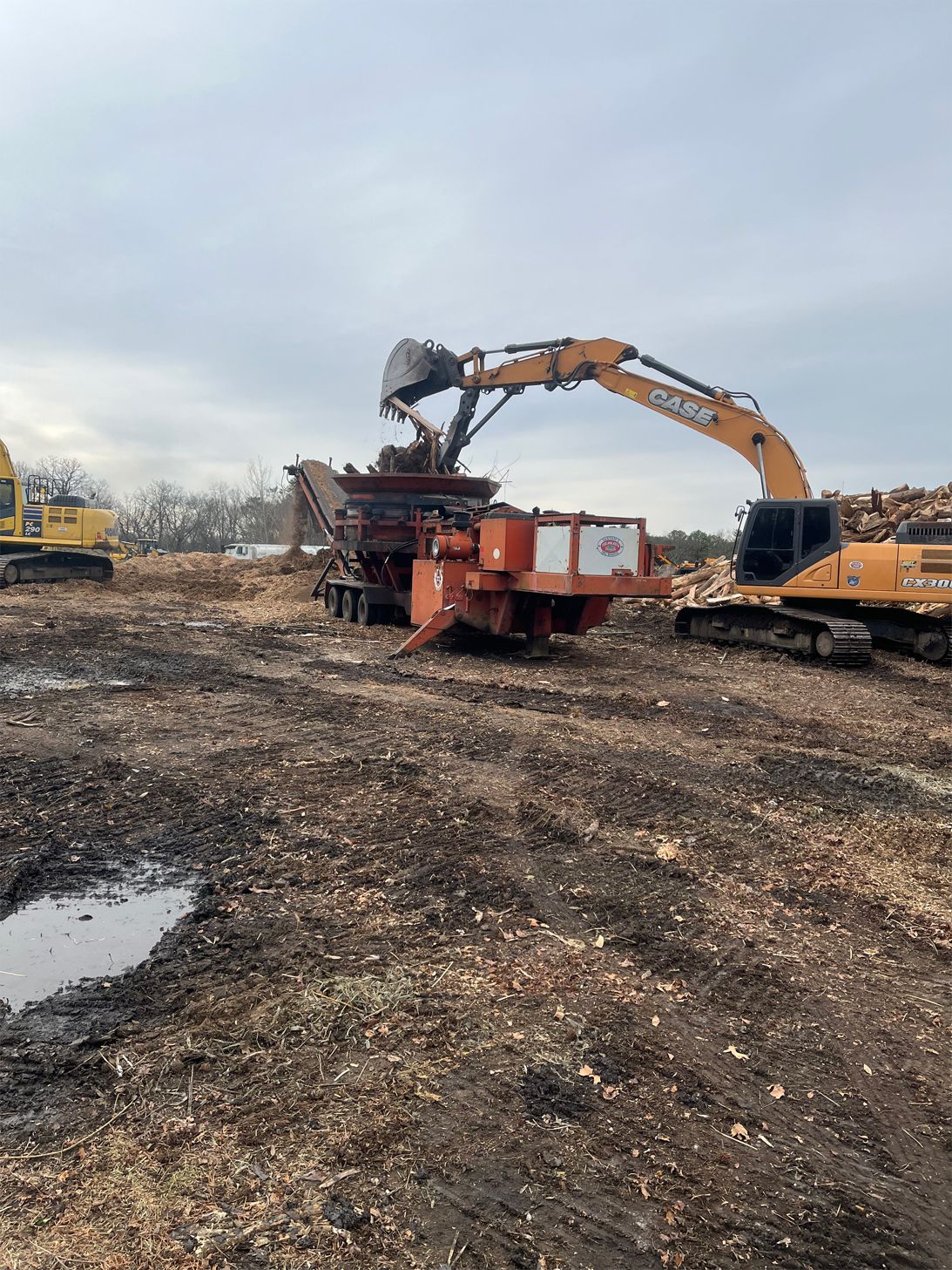 A large excavator is loading wood chips into a wood chipper.