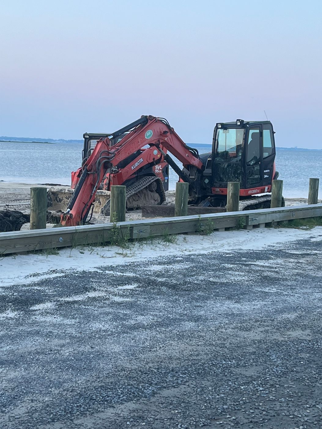A red excavator is sitting on the beach next to the ocean.