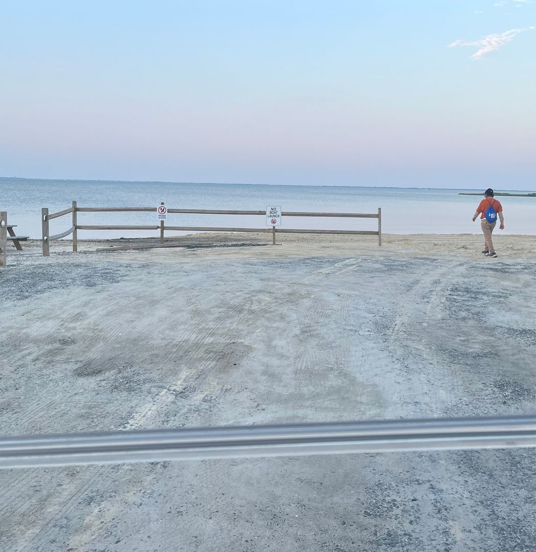 A person walking on a beach with a fence in the background