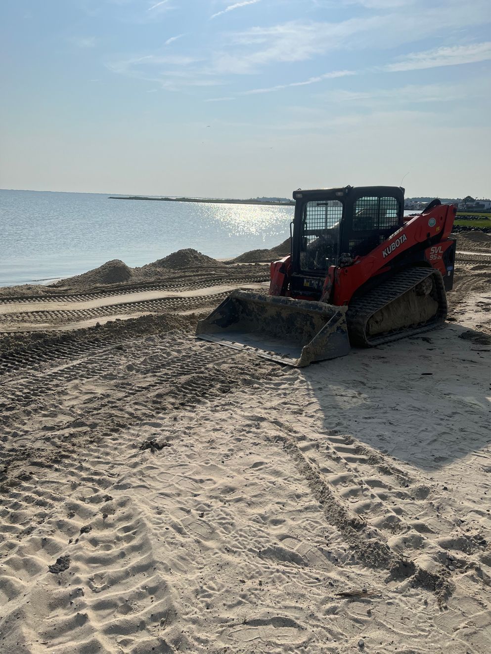 A bulldozer is sitting on top of a sandy beach next to the ocean.