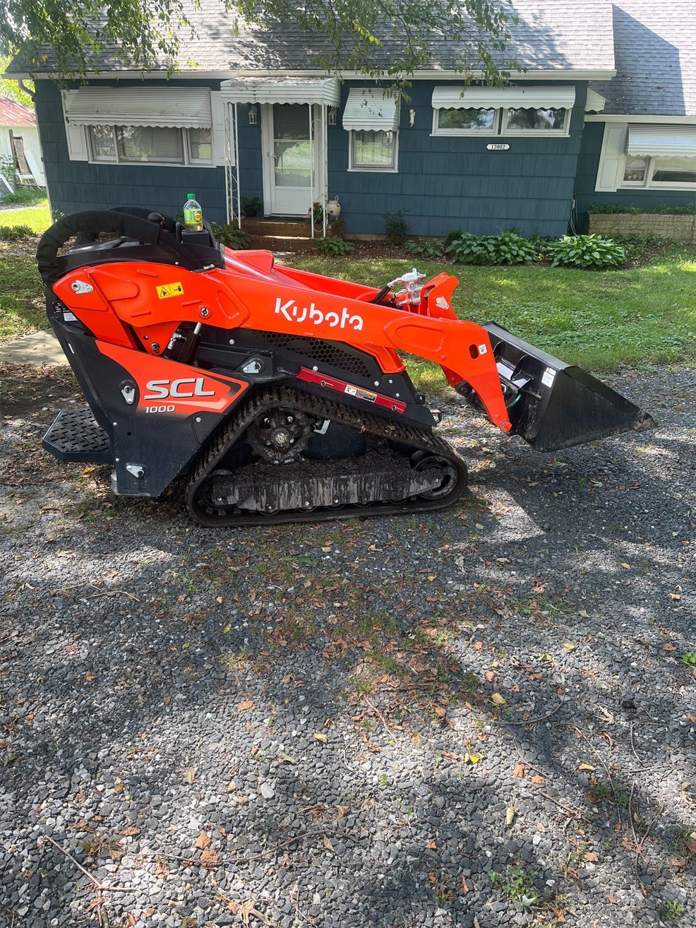 A small orange and black tractor is parked in front of a house.
