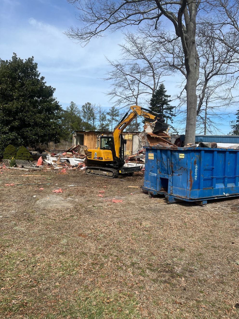 A yellow excavator is demolishing a house in a field.