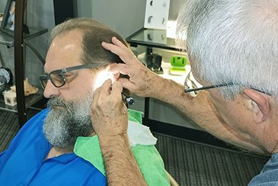 A man with glasses is getting his ears examined by another man.