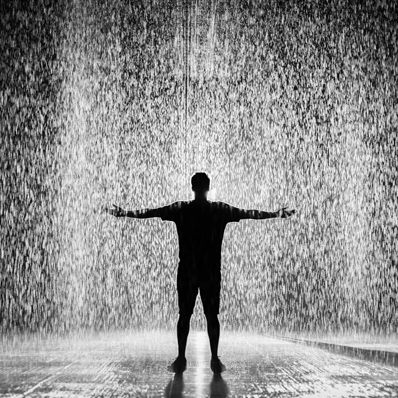 A man is standing in the rain with his arms outstretched.