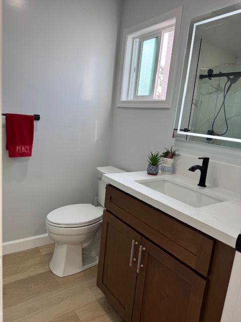 Bathroom with brown vanity, white countertop, toilet, mirror, and red towel.