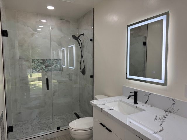 Modern bathroom with glass shower, lit mirror, white sink, and black fixtures.