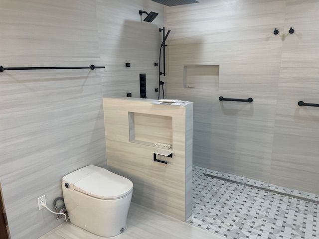 Modern, accessible bathroom with white tiled walls, black fixtures, and a seated toilet. Includes grab bars and a roll-in shower.