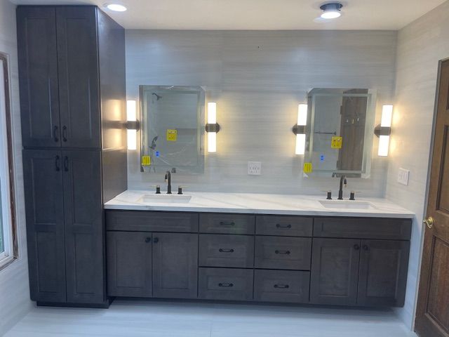 Bathroom with a long gray vanity, two mirrors with sconces, and tall storage cabinet.
