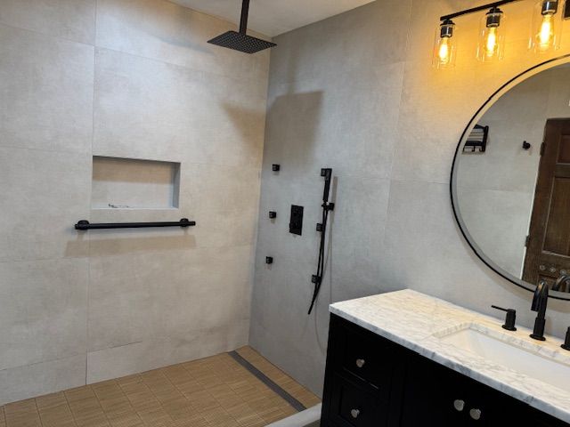 Modern bathroom with black fixtures, square rain showerhead, light gray tile, and a round mirror.