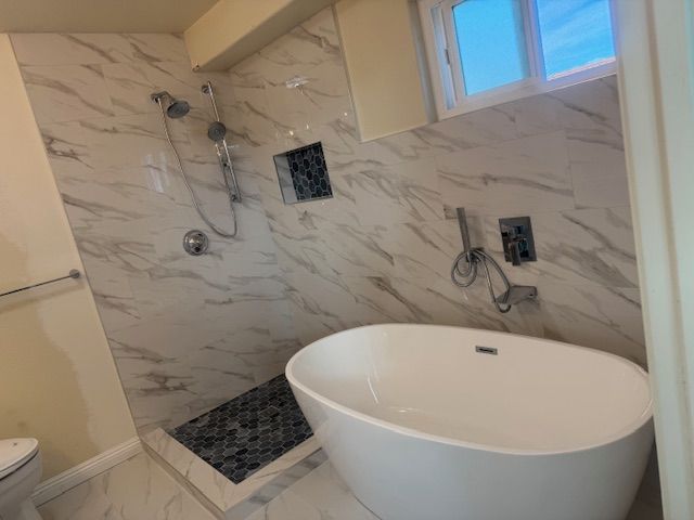 Bathroom with white marble tile shower, oval tub, and small window.