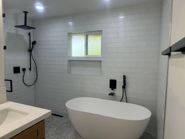 Modern white bathroom with freestanding tub, shower with black fixtures, window, and vanity.