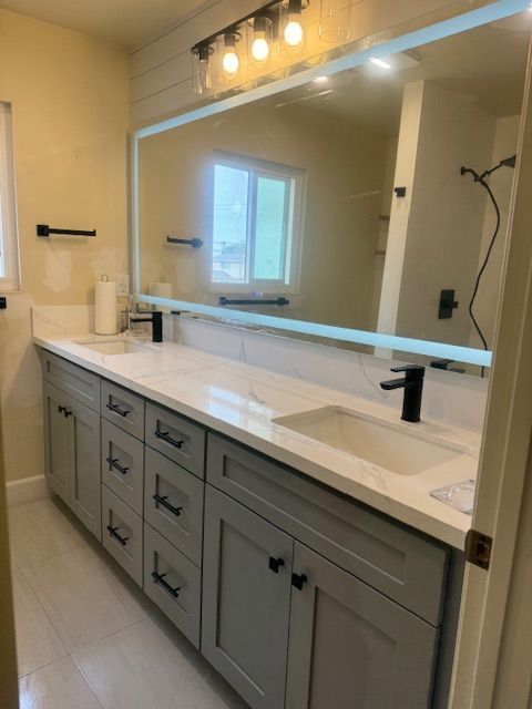 Gray bathroom vanity with white countertop, large mirror, and black fixtures.