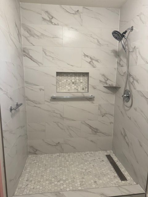 Tiled shower stall with white marble-patterned walls, pebble floor, and a built-in shelf.