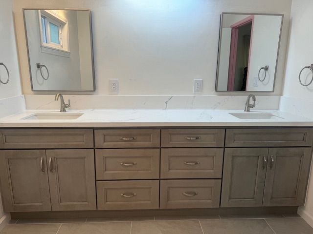 Gray bathroom vanity with two sinks, mirrors, and drawers.