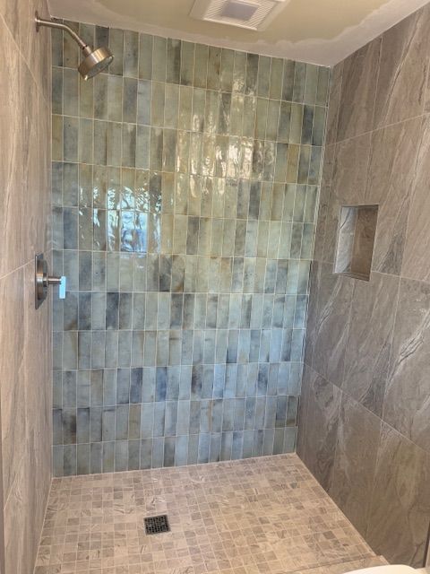 Shower with light green and grey tile walls, a built-in shelf, and a mosaic tile floor.