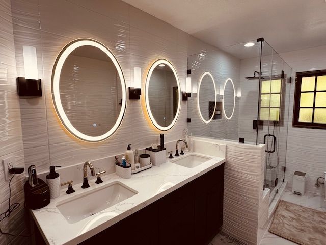 Modern bathroom with three oval mirrors, sconces, glass shower, and dark vanity.