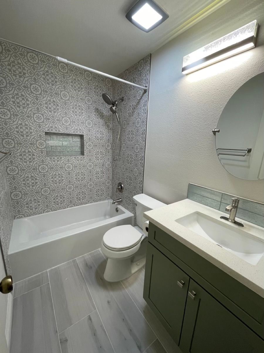 Bathroom with patterned tile shower, green vanity, and round mirror.