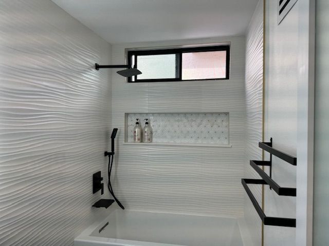 White bathroom with textured wave tiles, black shower fixtures, and a window.